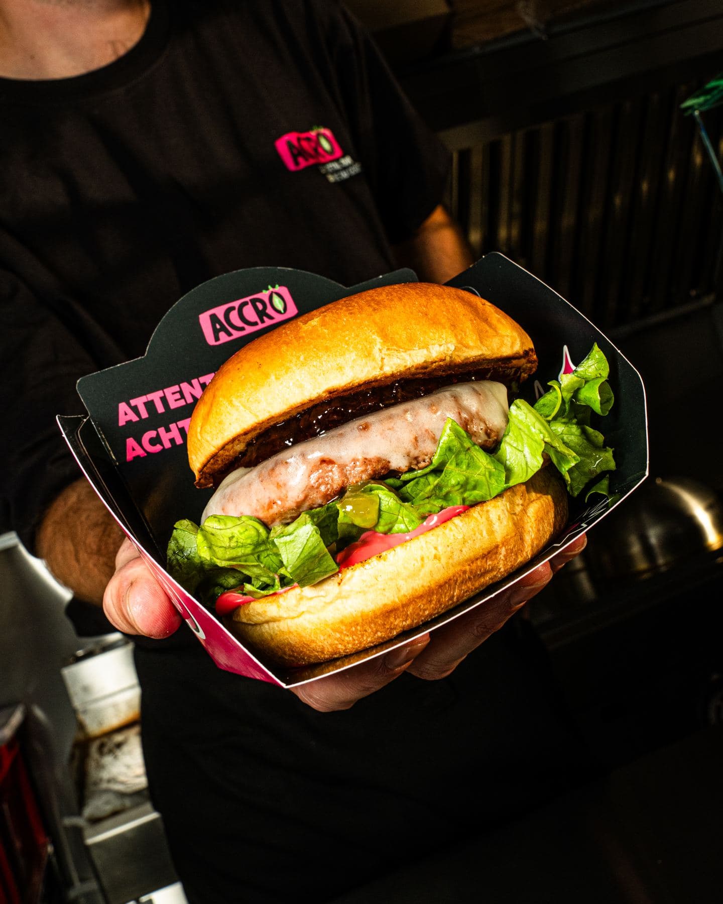 Un burger servi dans sa boîte, tendu depuis la cuisine d’une remorque food truck