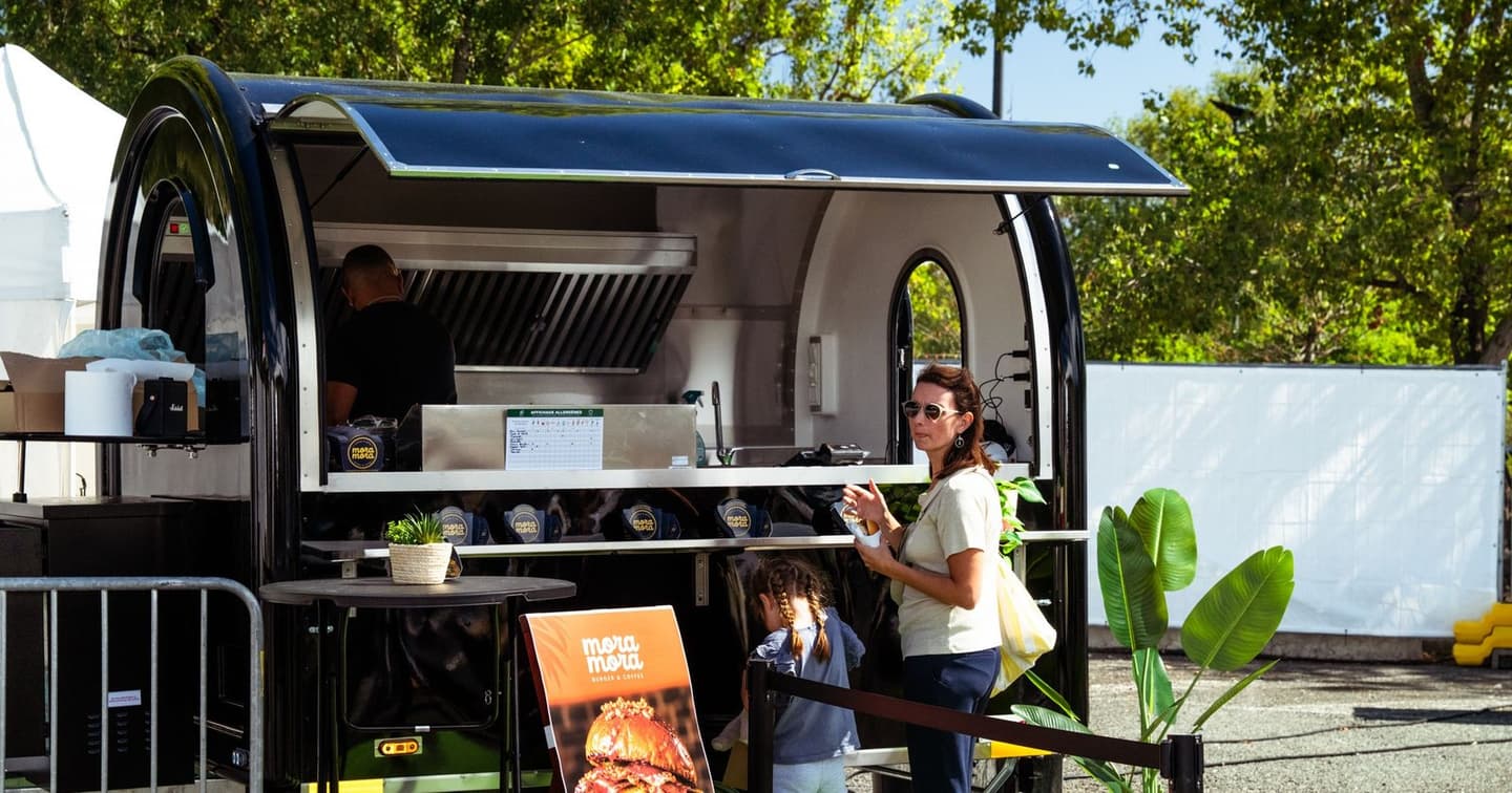 Une remorque food truck en service sur un festival, une cliente et sa fille devant le comptoir
