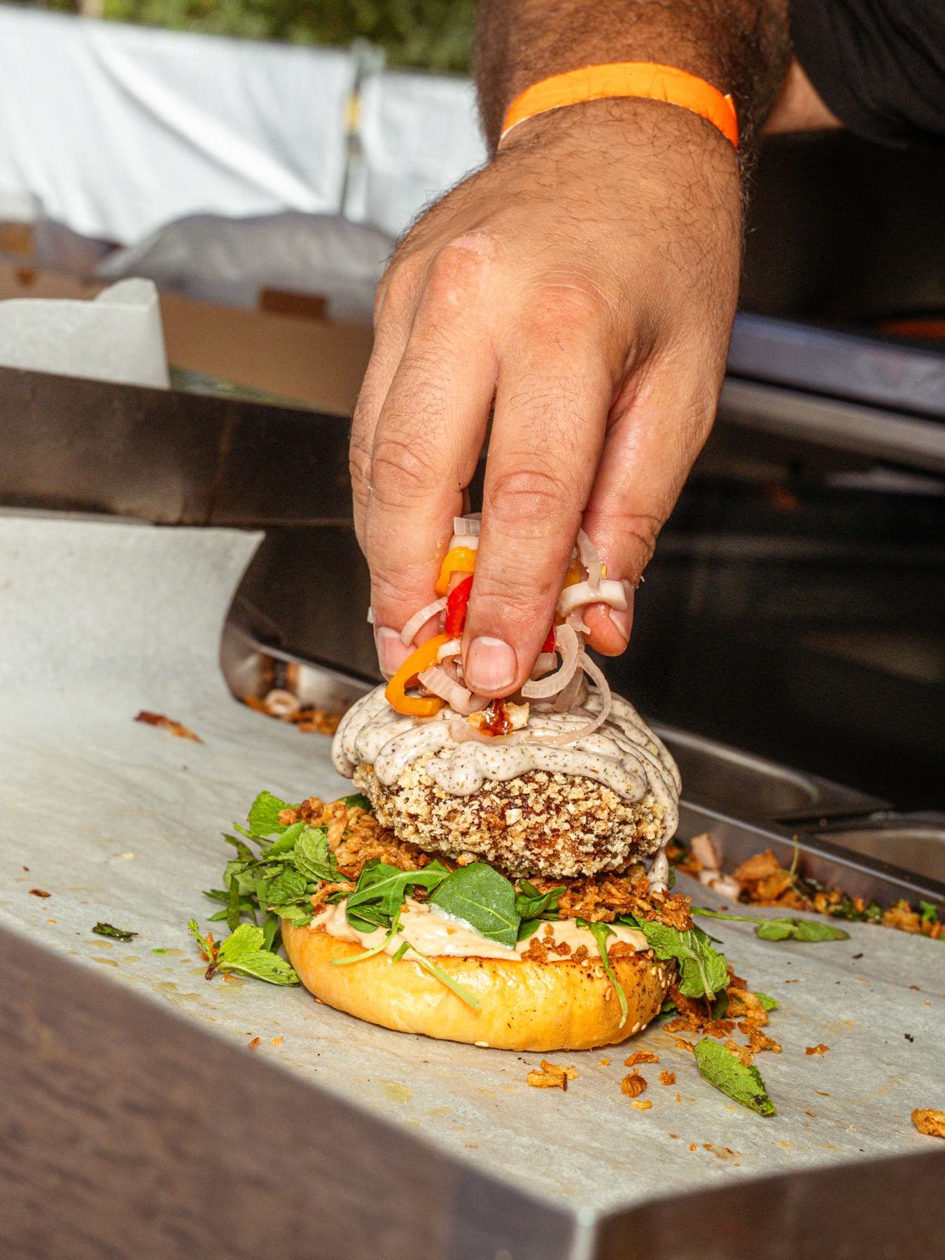 Hand legt die letzten Zutaten auf einen Burger, auf der Edelstahlfläche eines Food-Truck-Anhängers