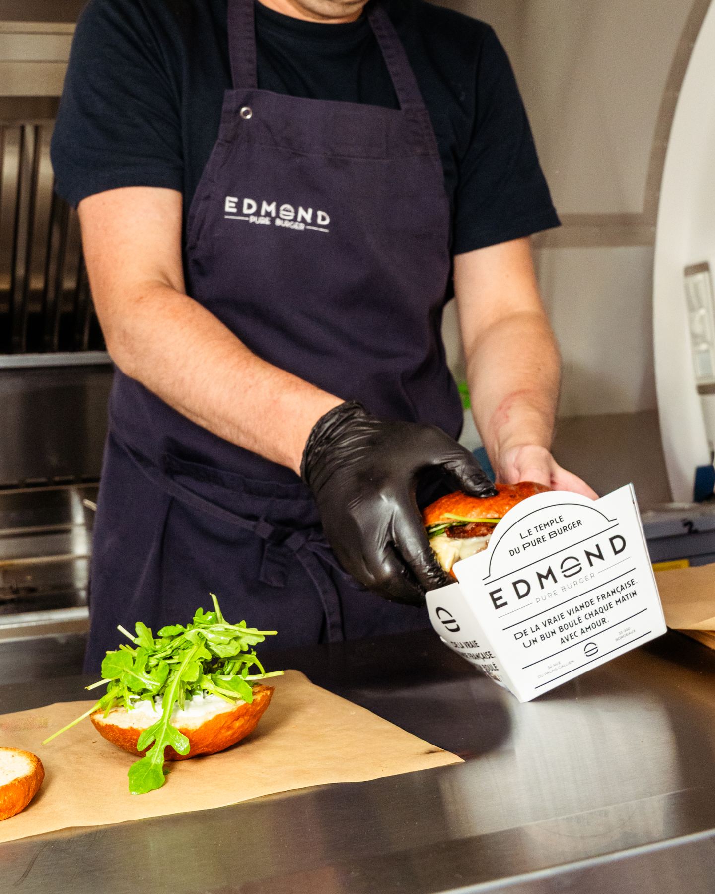 Un burger servi dans sa boîte par un cuisinier ganté